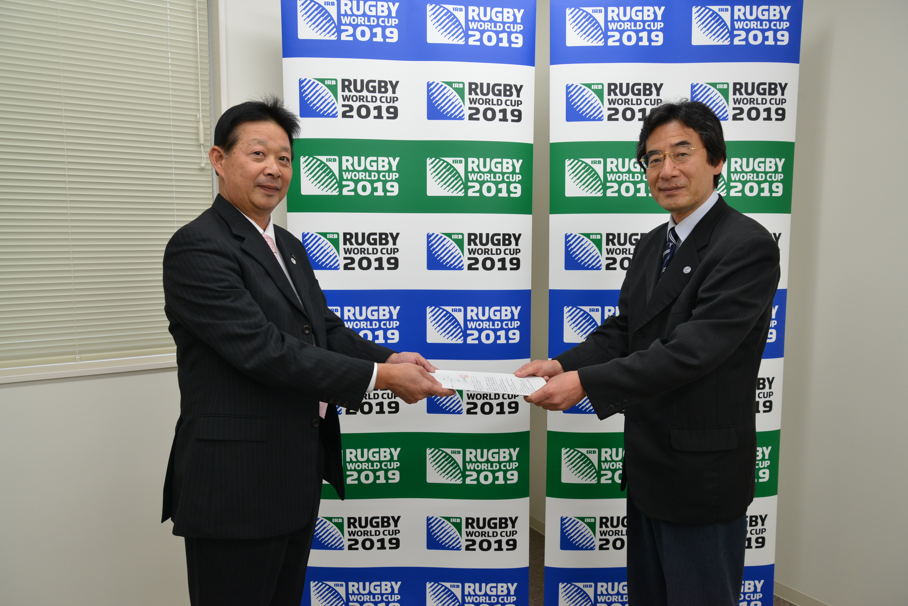 開催希望申請書を手渡す　左：栗橋ラグビーワールドカップ誘致室長　右：西阪組織委員会参与