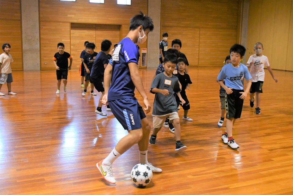 プロサッカー選手のドリブルからボールを奪おうとしている子ども