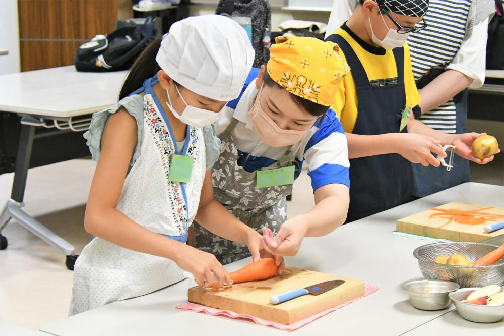 教えてもらいながら野菜を切る児童