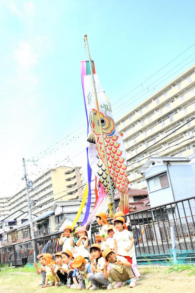 鯉のぼりの前で園児たちが集合写真を撮っている様子